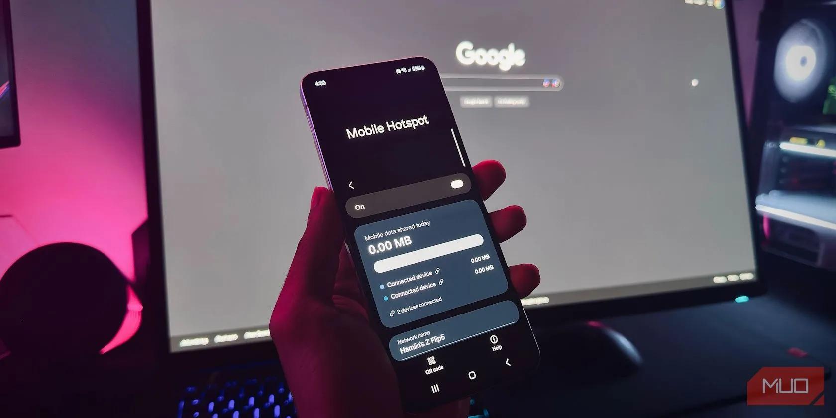 Bàn tay đang cầm điện thoại Android hiển thị cài đặt Điểm phát sóng di động (Mobile Hotspot) trước màn hình máy tính