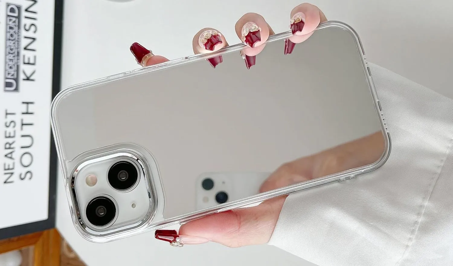 Bàn tay đang cầm một chiếc iPhone được trang bị ốp lưng gương phản chiếu.