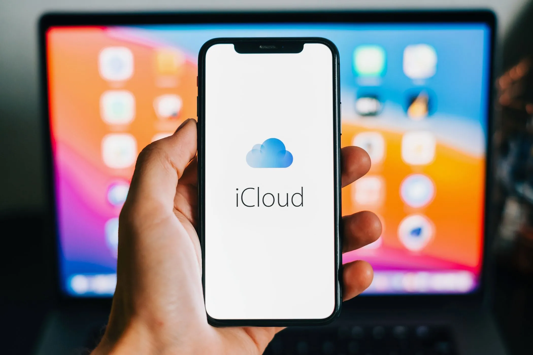 Biểu tượng iCloud hiển thị trên iPhone với MacBook trong nền, minh họa sự tích hợp hệ sinh thái Apple