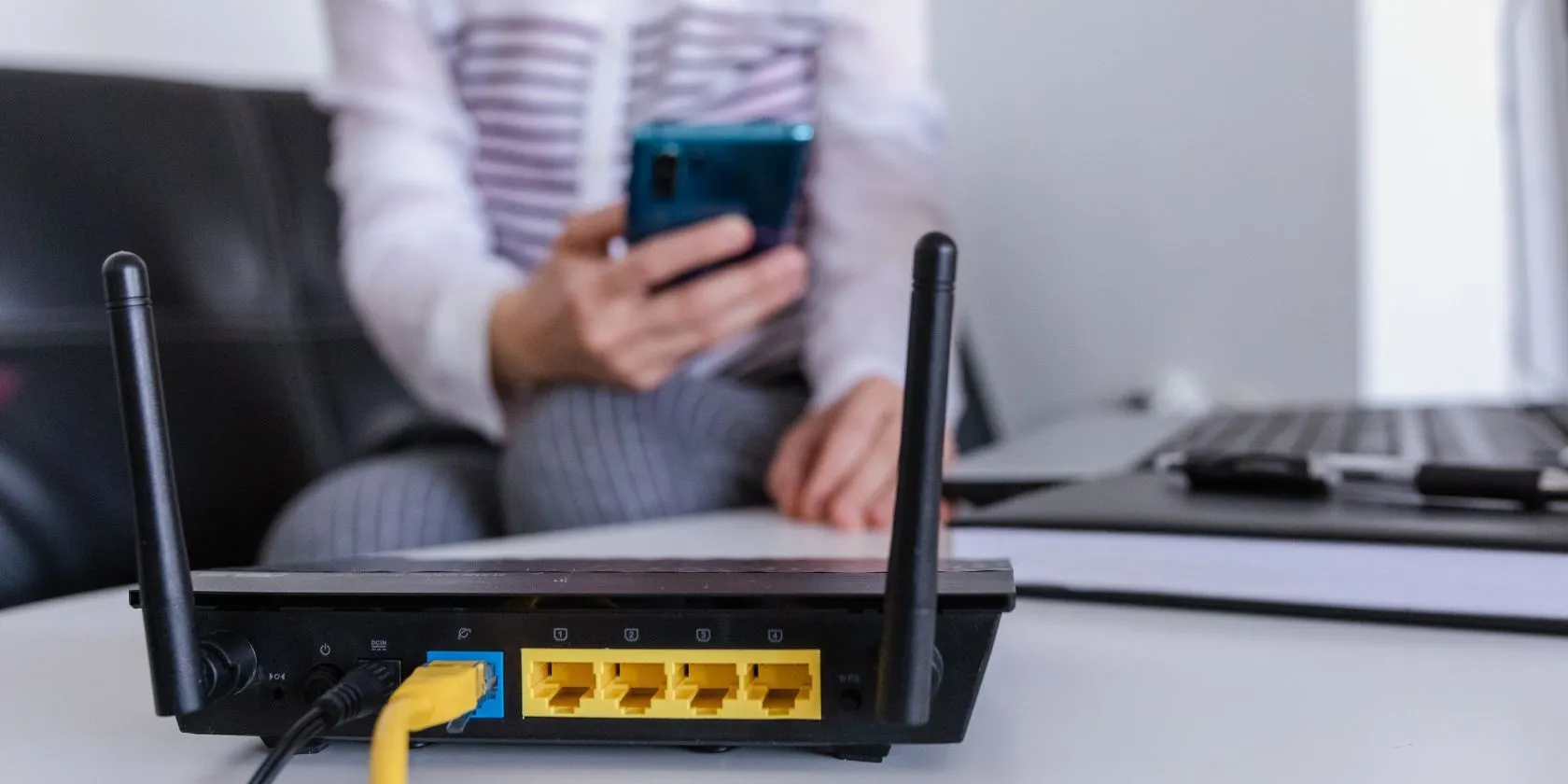 Bộ định tuyến Wi-Fi đặt trước nền một người đang sử dụng thiết bị, thể hiện sự kết nối mạng gia đình.