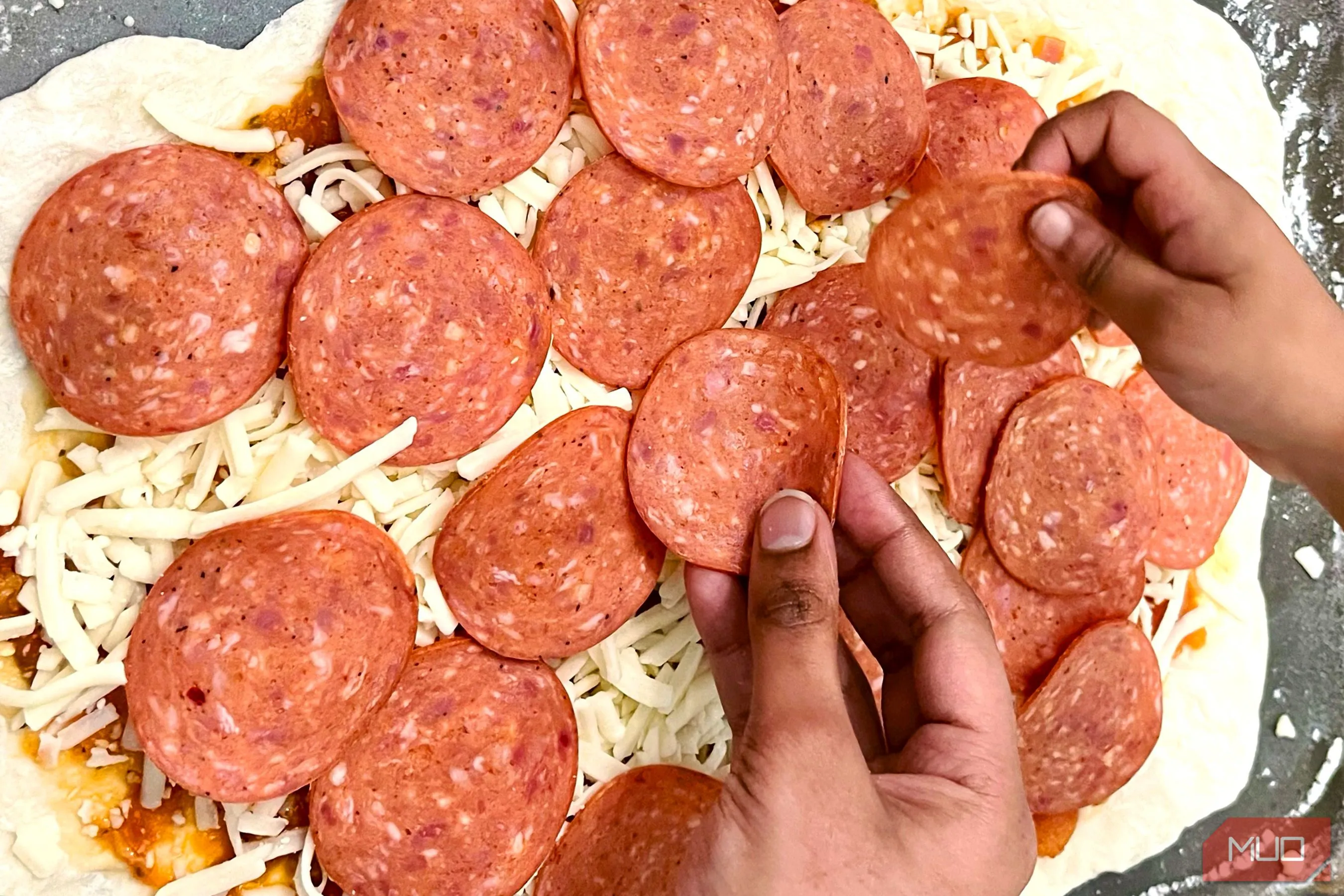 Đôi bàn tay đang đặt các nguyên liệu lên bánh pizza, tạo yếu tố con người và kể câu chuyện về quá trình làm bánh.