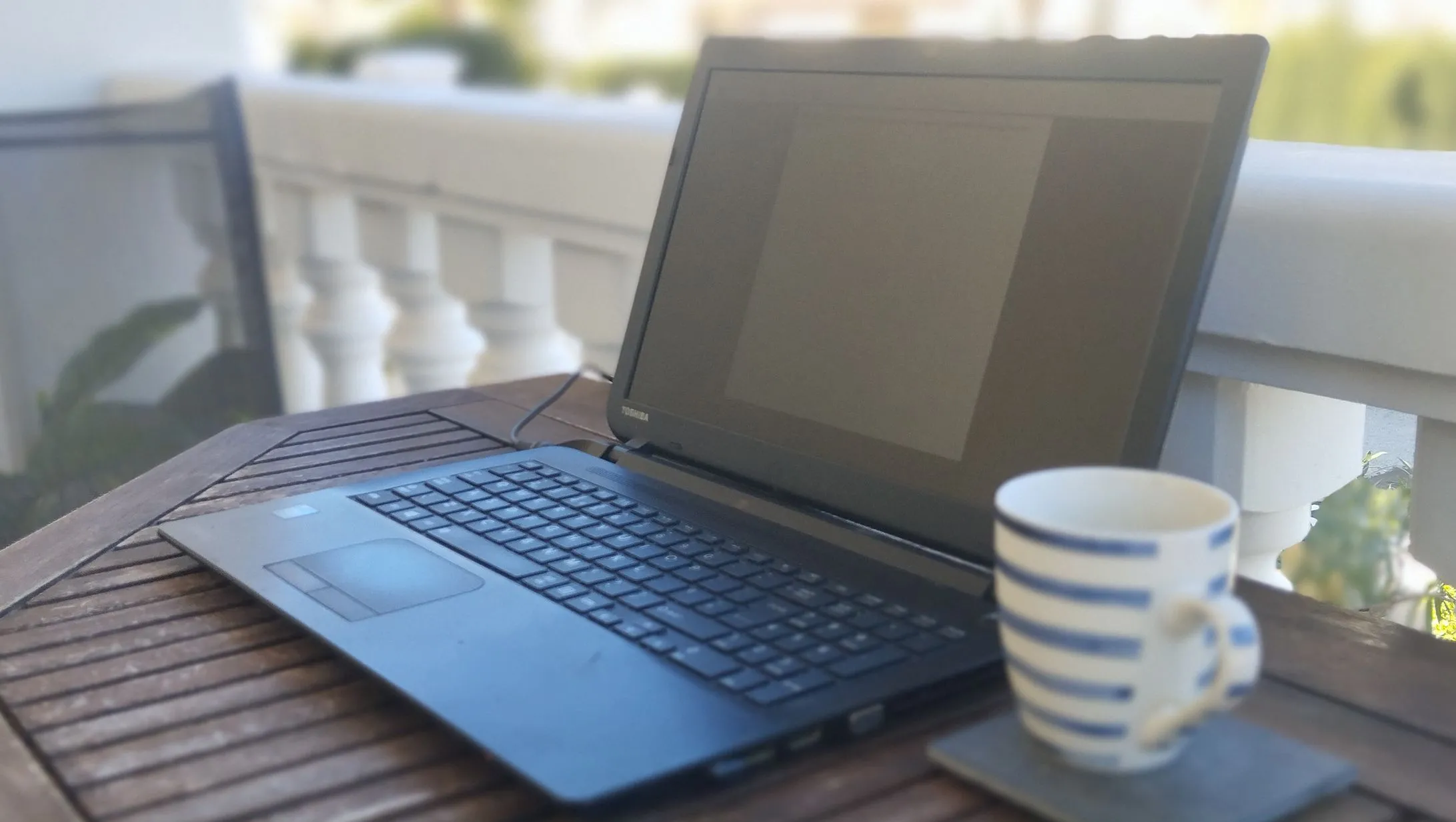 Hình ảnh một chiếc laptop Toshiba cũ đặt trên bàn cạnh cốc cà phê, thể hiện không gian làm việc tập trung