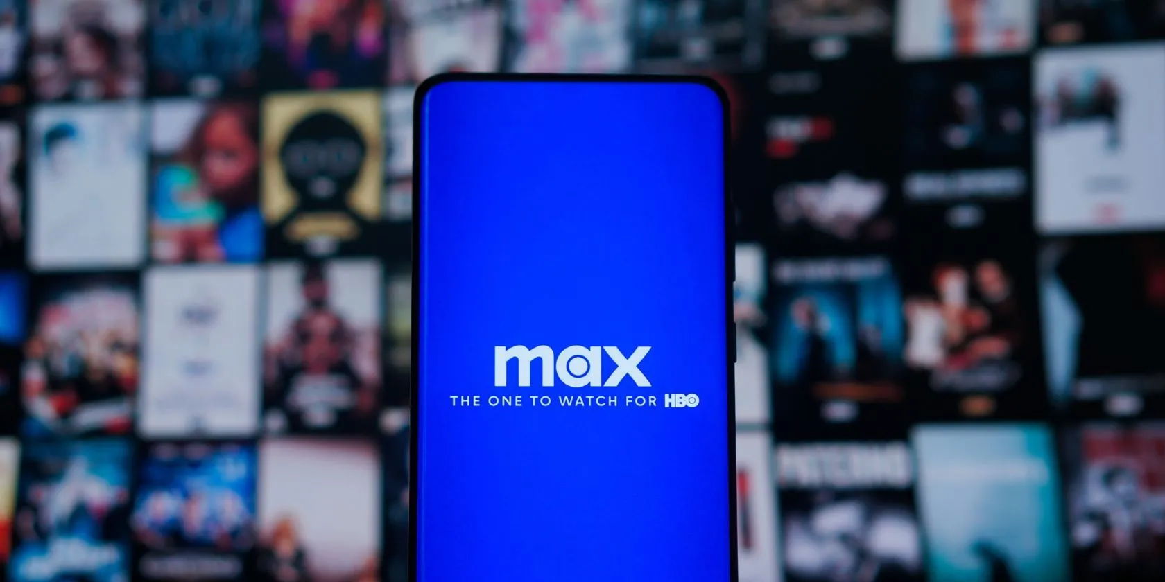 Logo Max trên điện thoại thông minh, phía sau là màn hình TV hiển thị nội dung, tượng trưng cho dịch vụ streaming Max