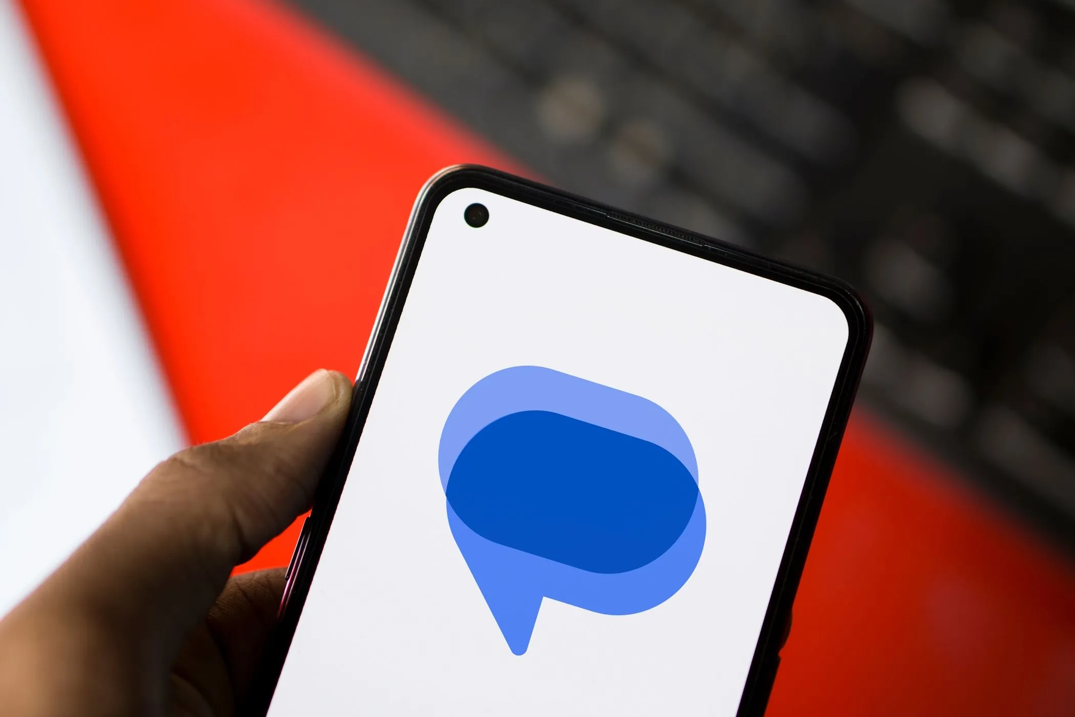 Logo ứng dụng Google Messages hiển thị trên màn hình điện thoại Android, có bàn phím ảo ở phía sau