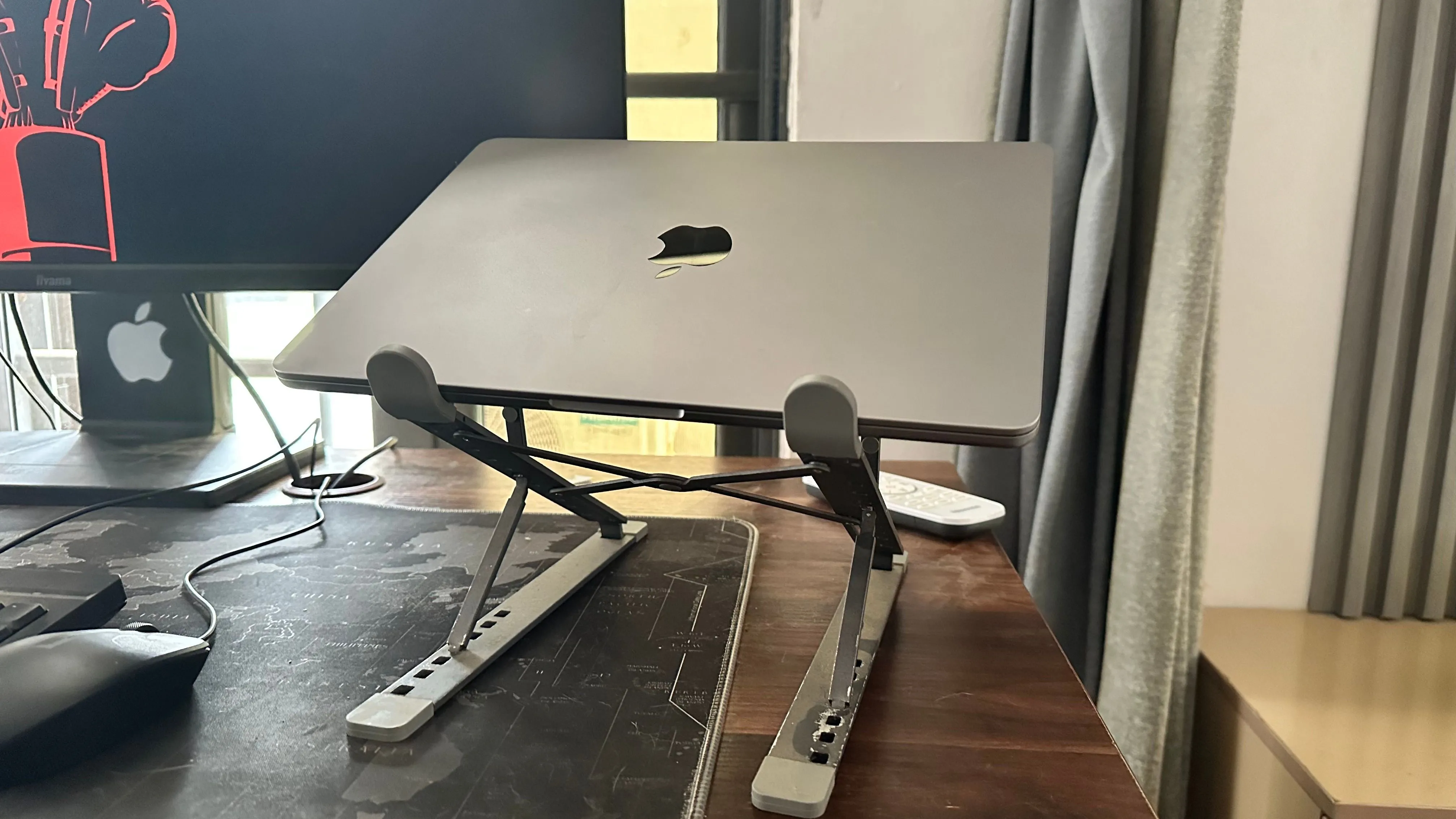 MacBook đặt trên giá đỡ cạnh màn hình ngoài, cho thấy sự kết hợp thường thấy nhưng có thể ảnh hưởng đến tuổi thọ pin.