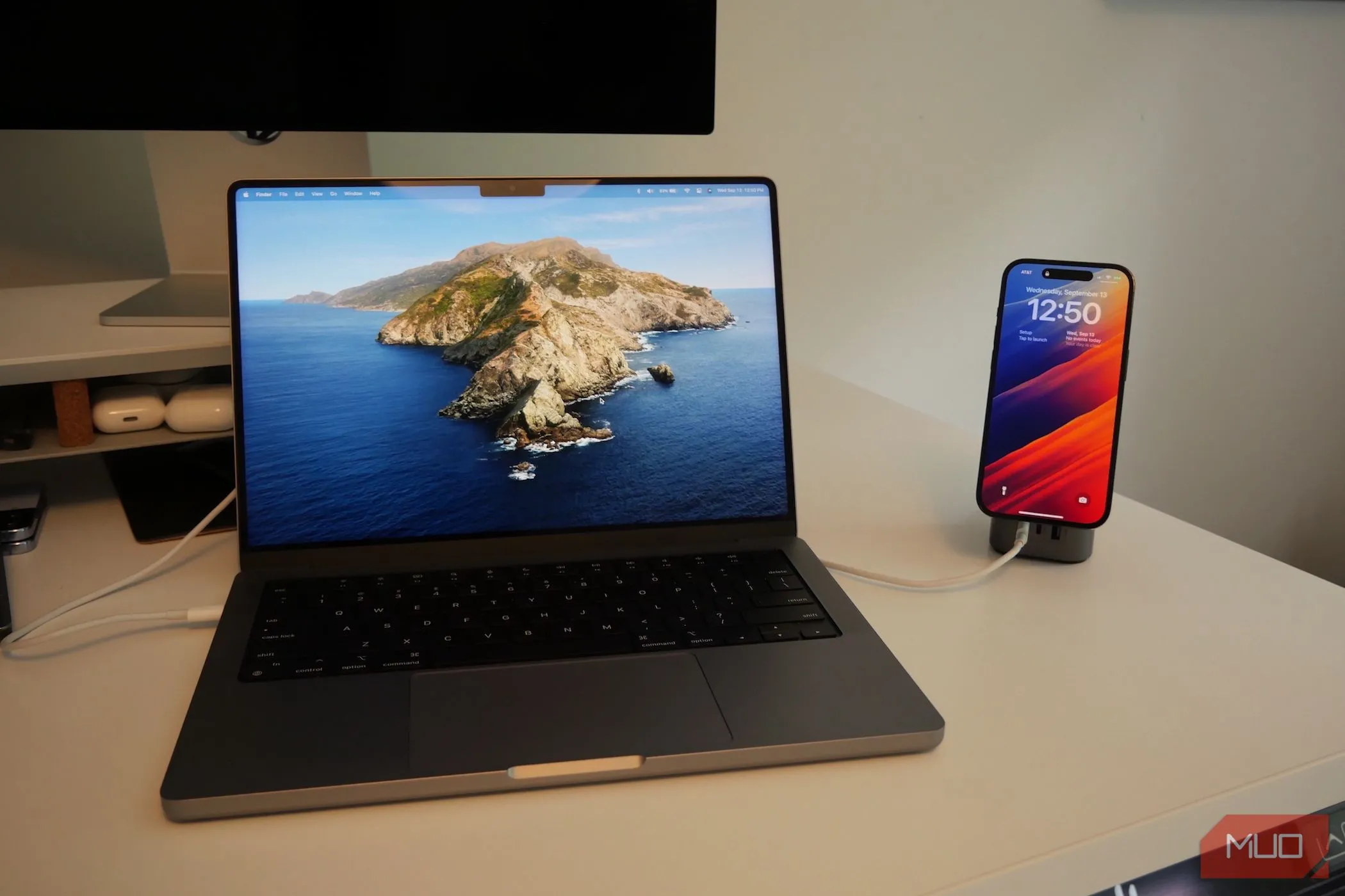 MacBook Pro và iPhone đang sạc trên bàn, thể hiện sự kết nối giữa hai thiết bị của Apple