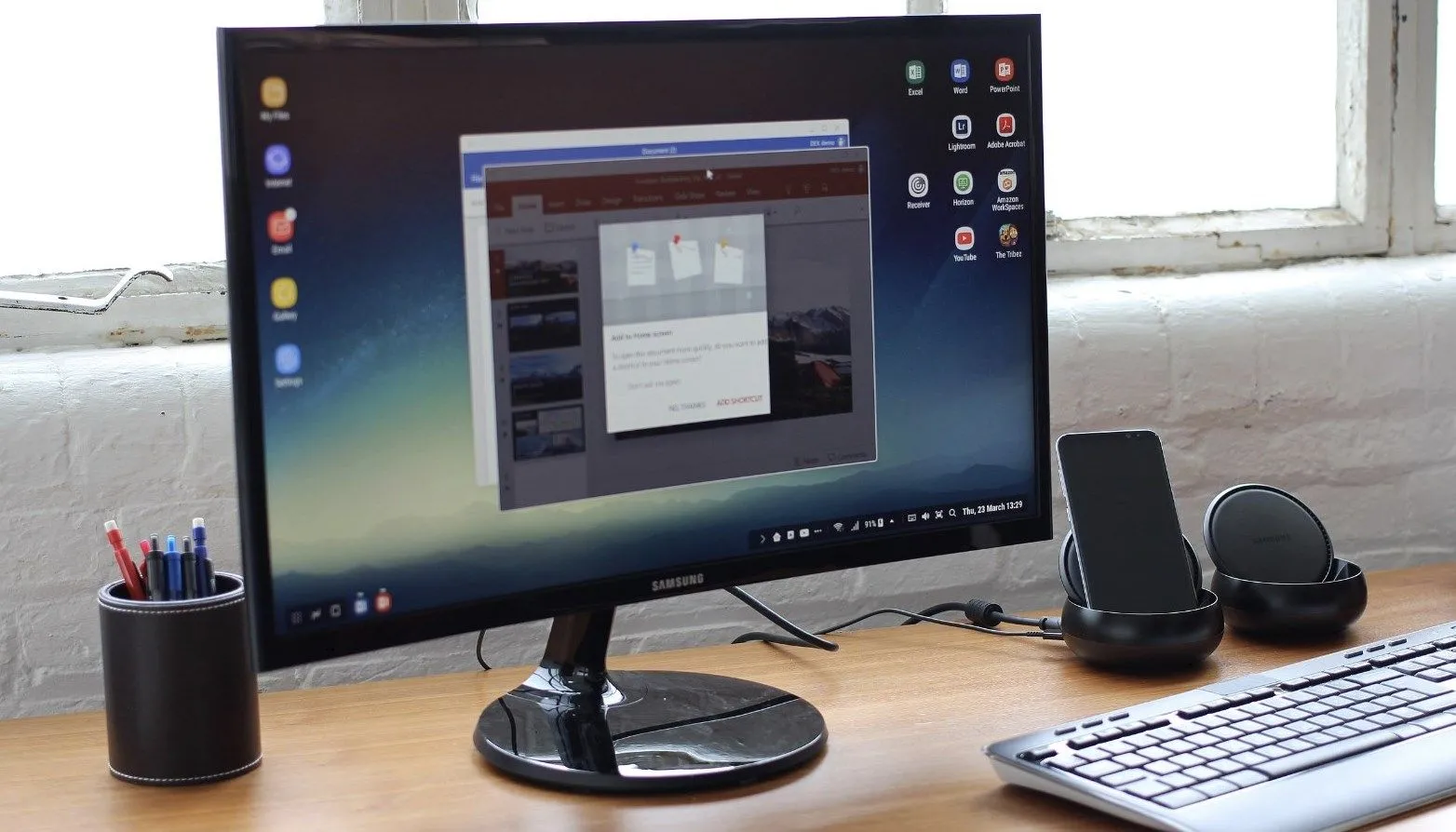 Màn hình Samsung đang hiển thị giao diện DeX, đặt trên bàn làm việc cùng với bàn phím và hệ thống âm thanh.