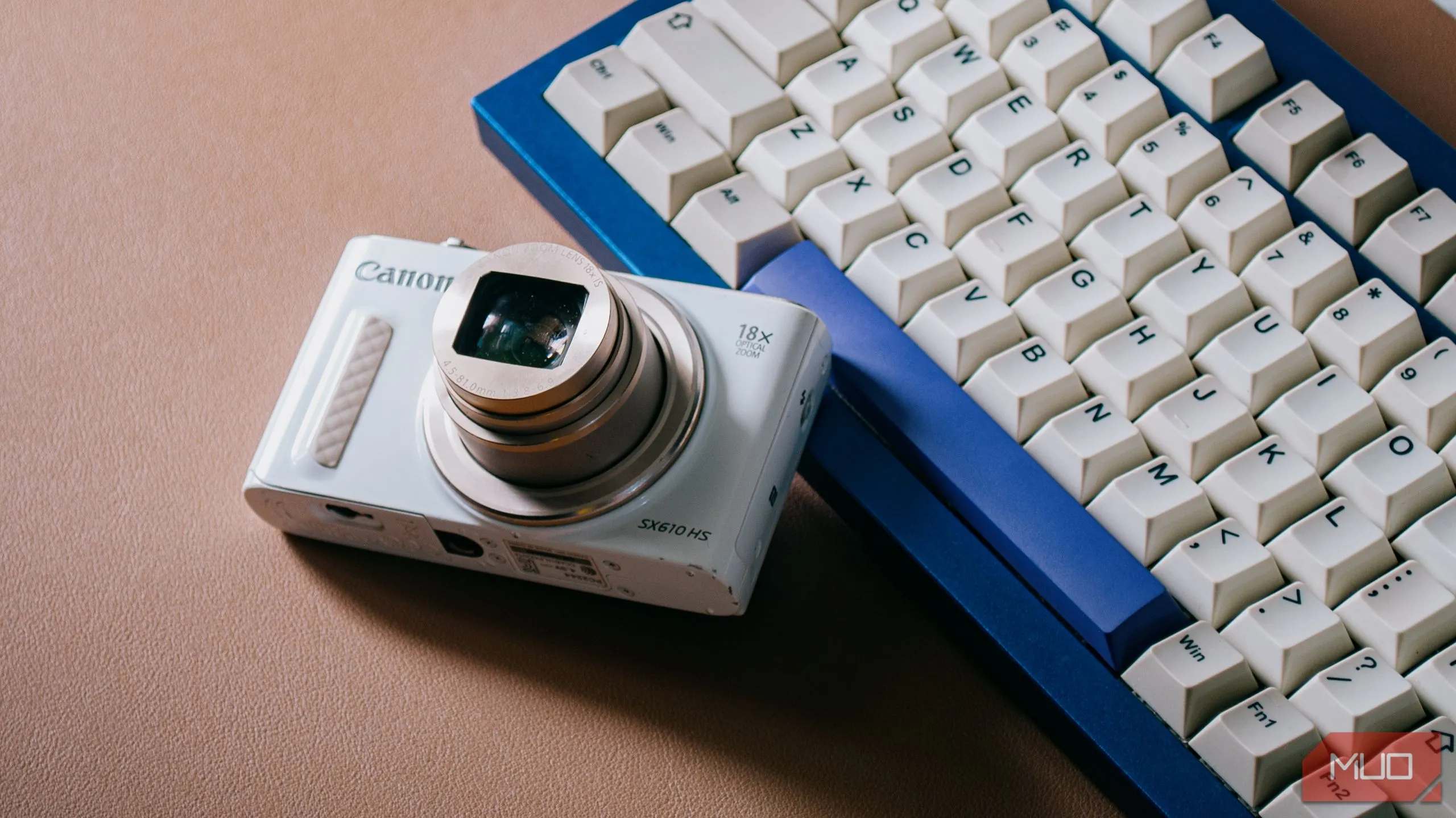 Máy ảnh kỹ thuật số nhỏ gọn (digicam) với ống kính đang nhô ra, đặt trên bàn phím máy tính.