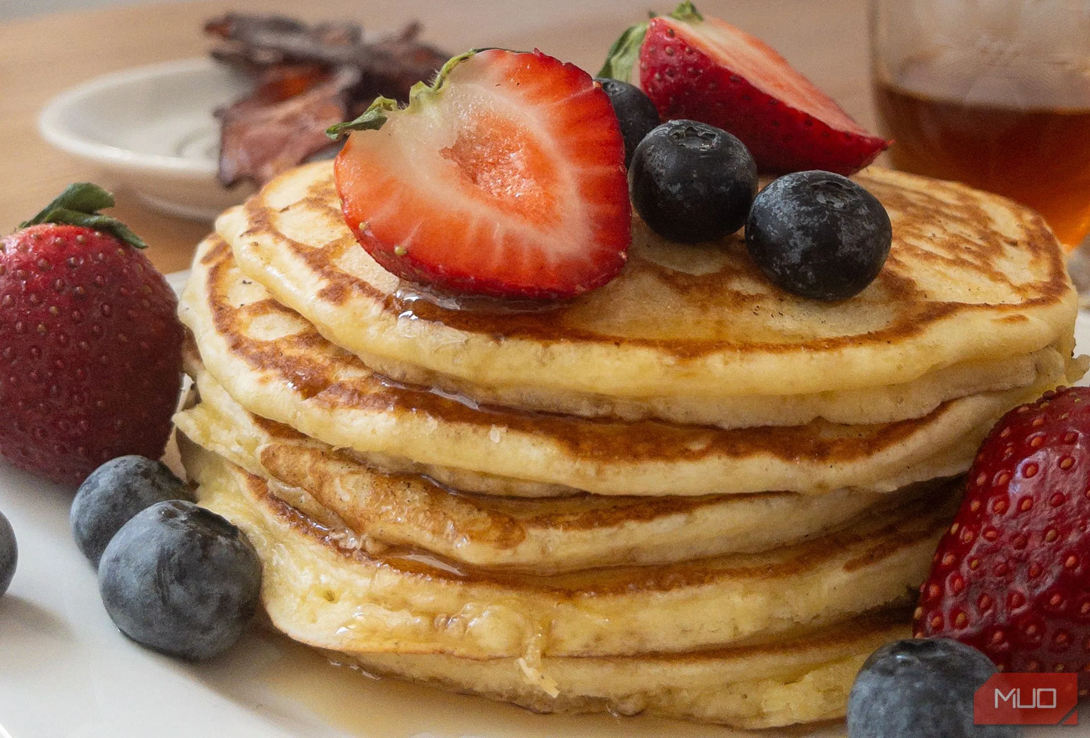 Món bánh pancake xếp chồng với quả mọng và si-rô, chụp từ trên xuống (flat lay) làm nổi bật sự phong phú của bữa sáng.