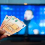 Một bàn tay cầm tiền trước màn hình TV