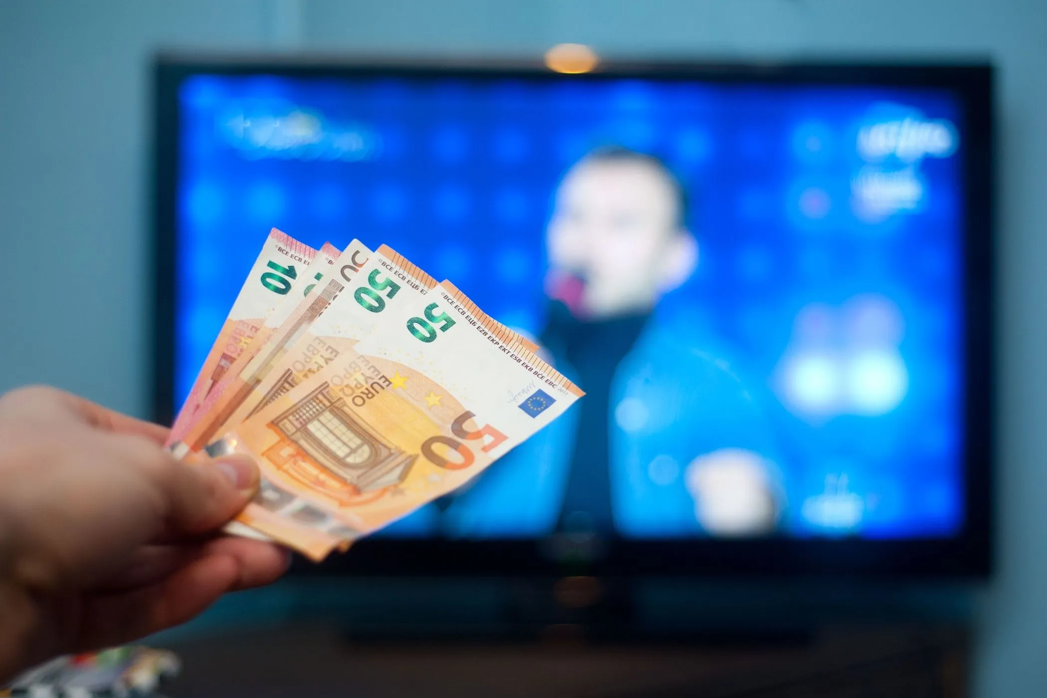 Một bàn tay cầm tiền trước màn hình TV