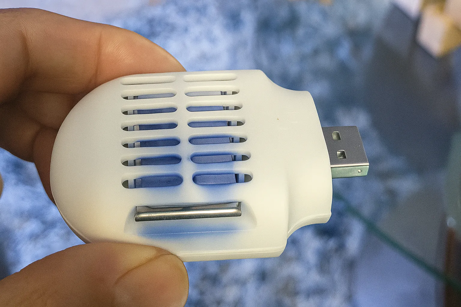 Một bàn tay đang cầm máy đuổi muỗi Moskiller USB nhỏ gọn màu trắng.