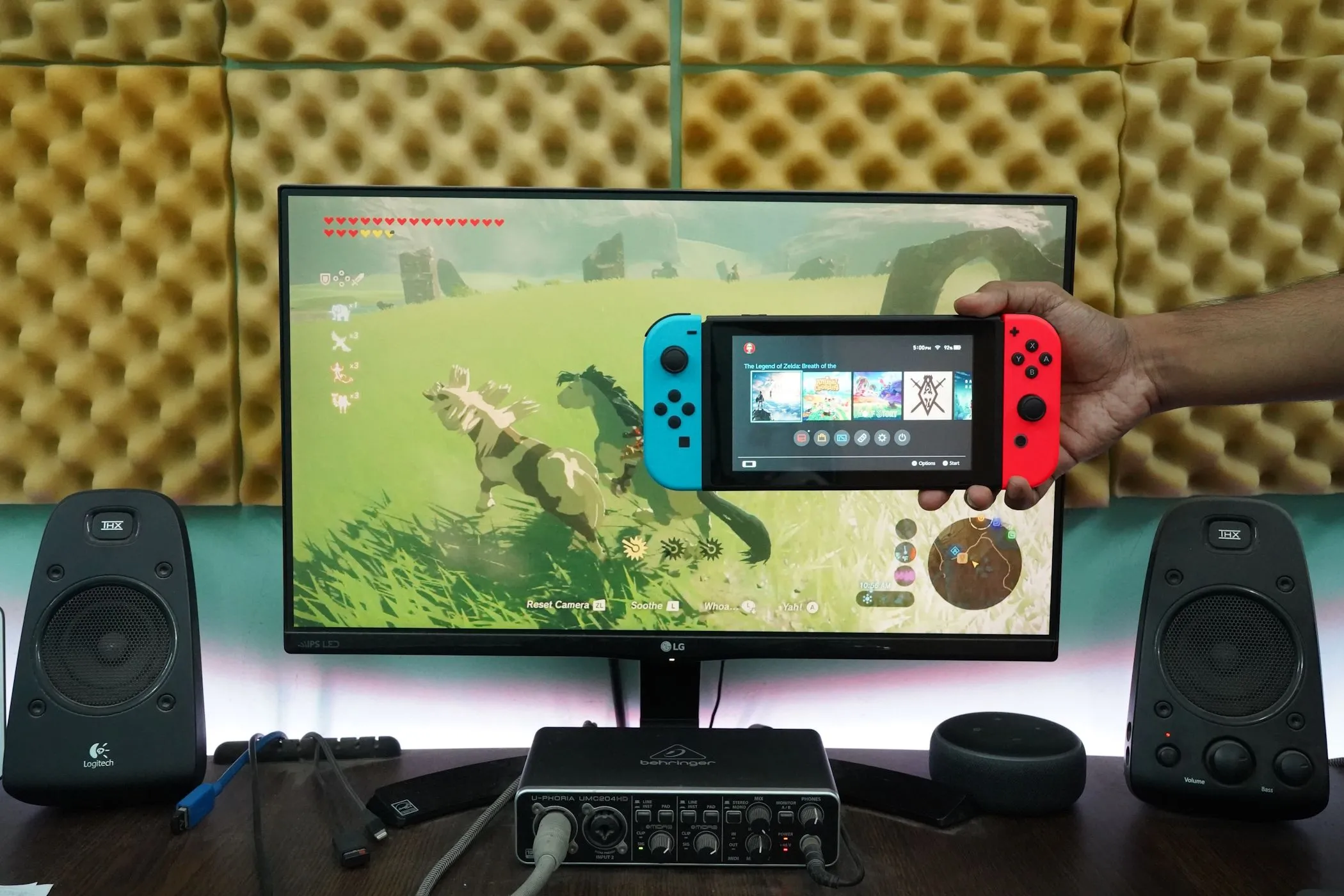 Một người đàn ông đang cầm máy chơi game Nintendo Switch phía trước một màn hình máy tính.