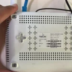 Một người đang cầm router Wi-Fi và chỉ vào mặt sau, nơi thường có thông tin đăng nhập mặc định