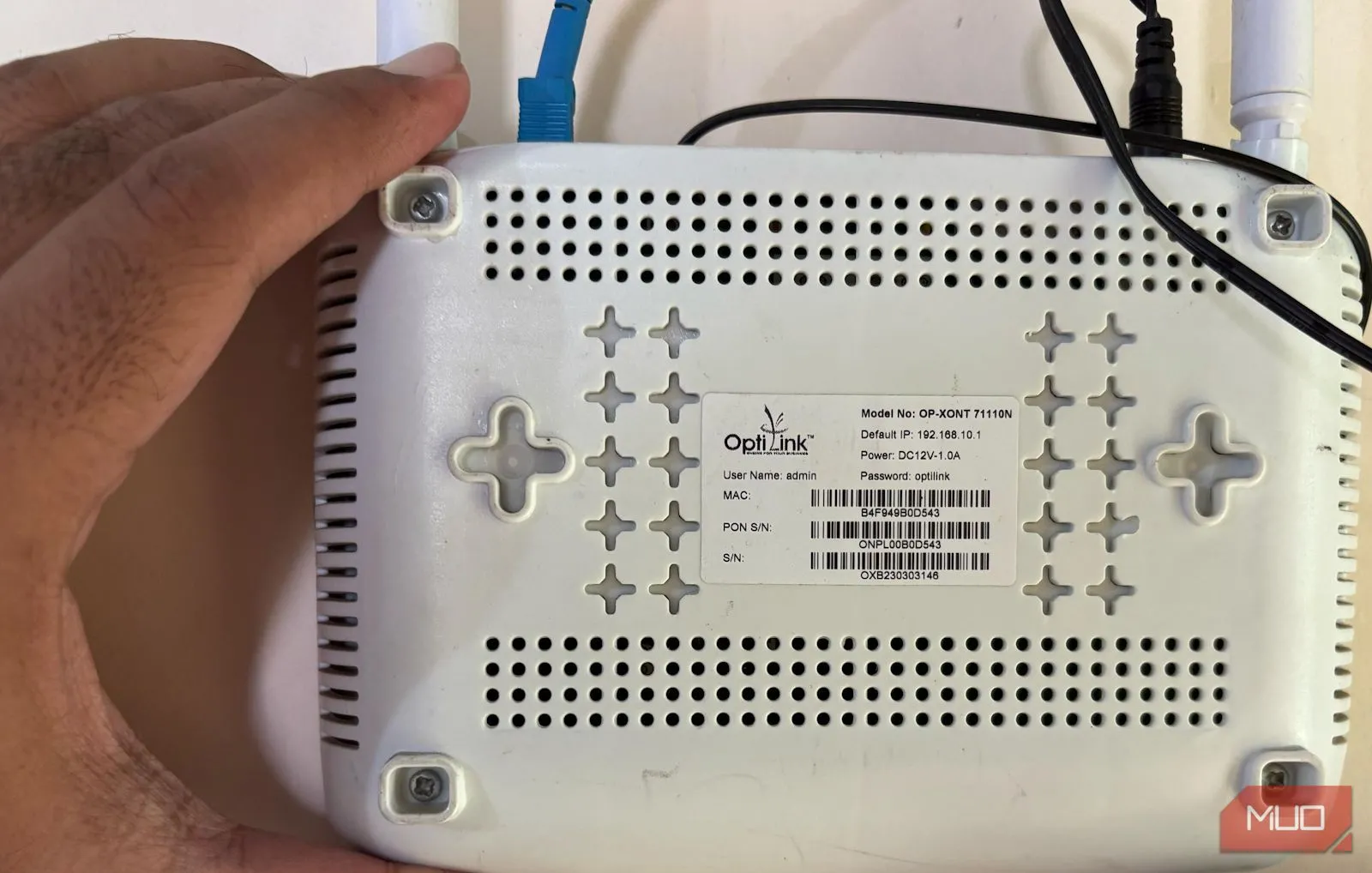Một người đang cầm router Wi-Fi và chỉ vào mặt sau, nơi thường có thông tin đăng nhập mặc định