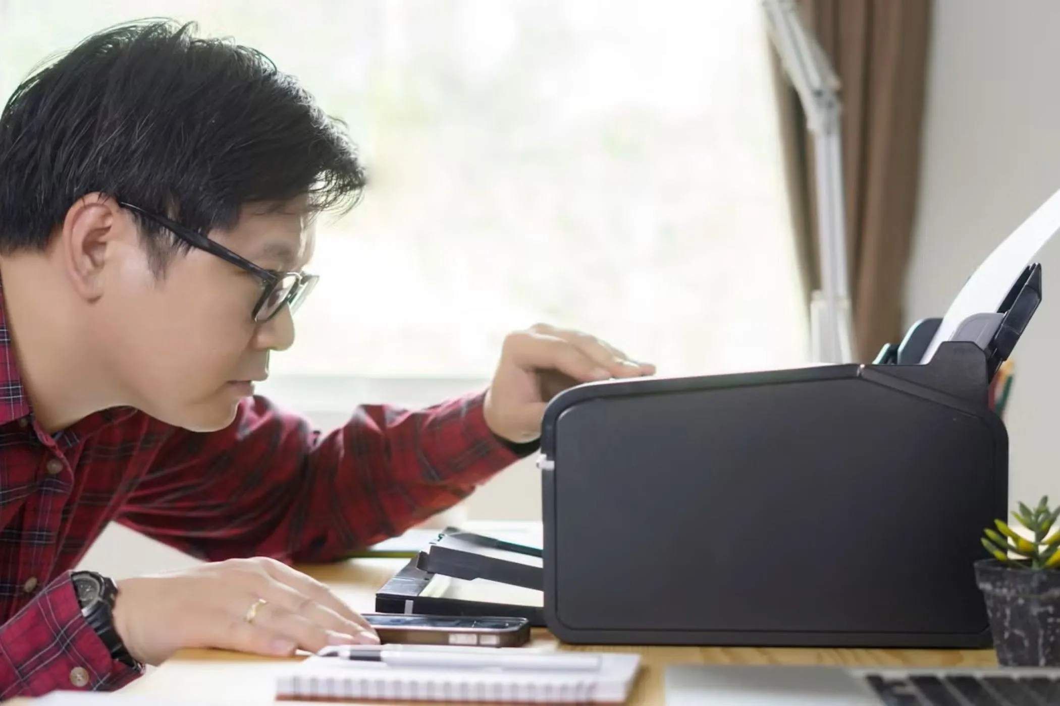 Người đàn ông đang kiểm tra máy in trên bàn làm việc, biểu cảm lo lắng về lỗi in ấn.
