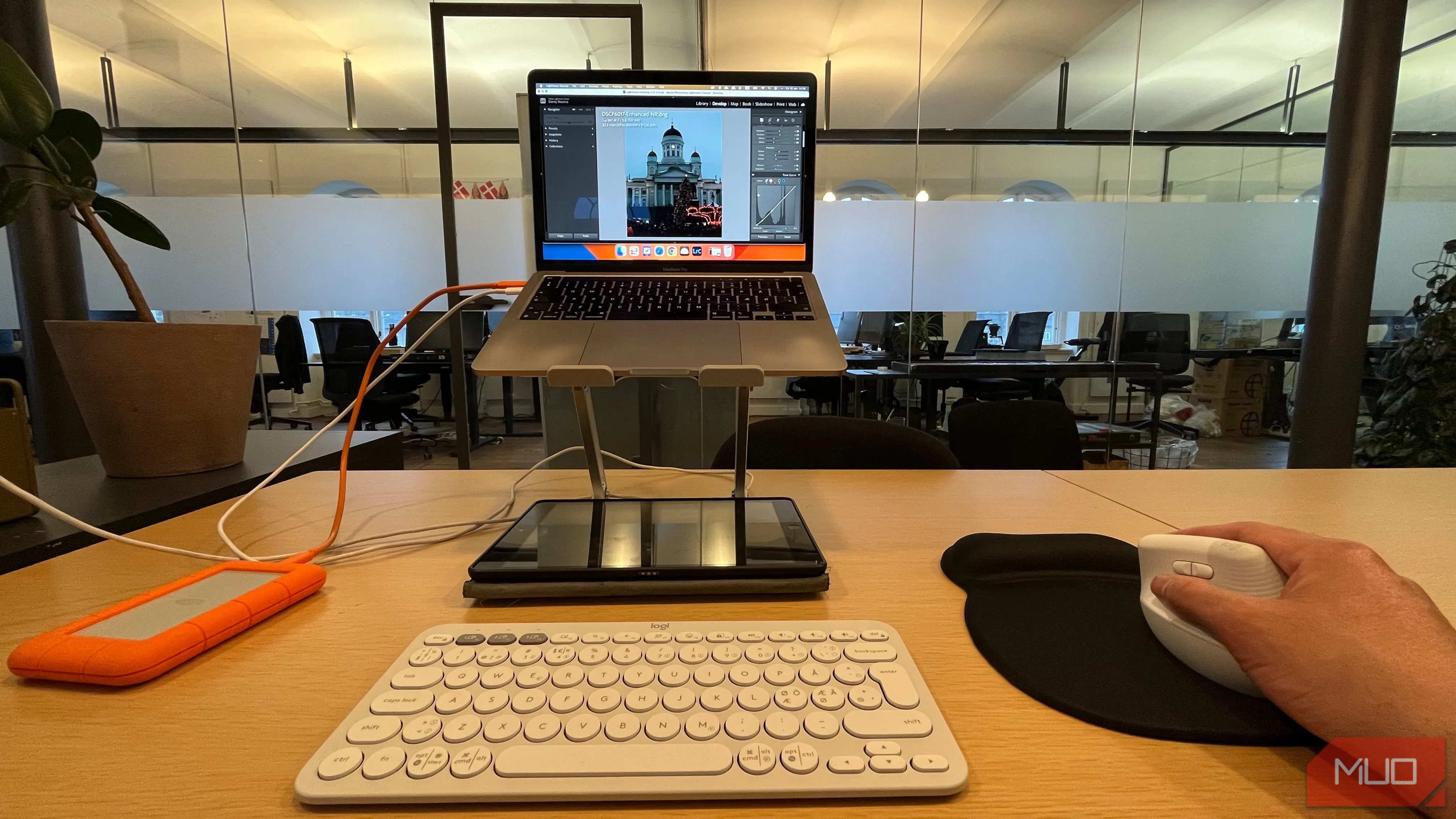 Người dùng đang chỉnh sửa ảnh trên laptop đặt trên giá đỡ, sử dụng chuột không dây
