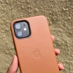 Ốp lưng da iPhone 12 màu nâu be trong tay, tường ở phía sau