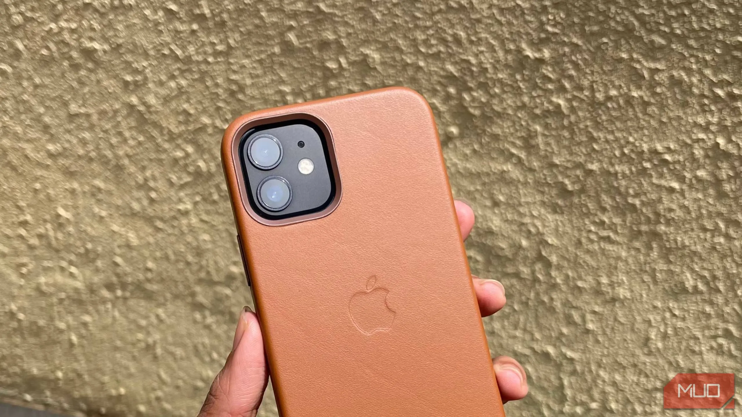 Ốp lưng da iPhone 12 màu nâu be trong tay, tường ở phía sau