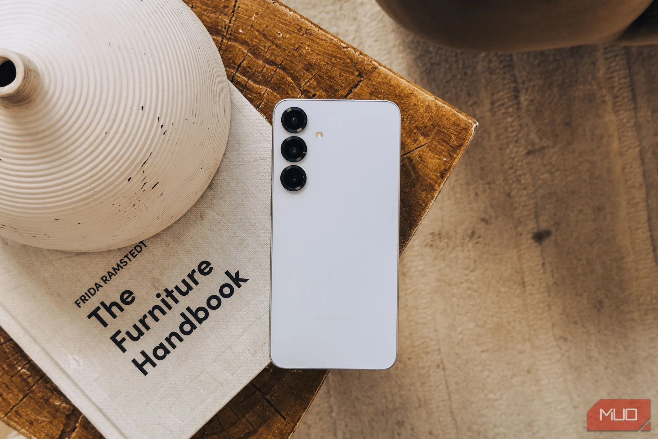 Samsung Galaxy S25 màu bạc đặt trên cuốn sách trắng, thể hiện thiết kế camera